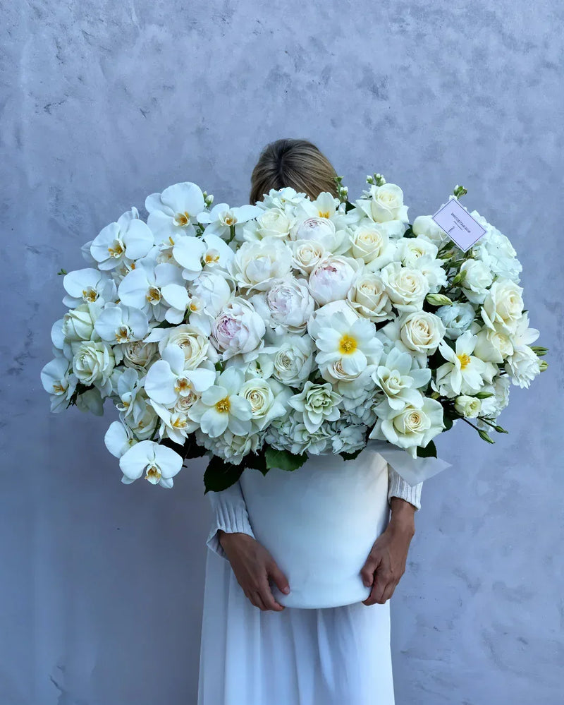Person holding a large bouquet of white flowers against a plain background