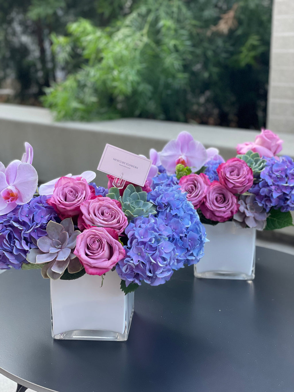 Arreglo floral con orquídea y suculentas en jarrón cuadrado de vidrio.