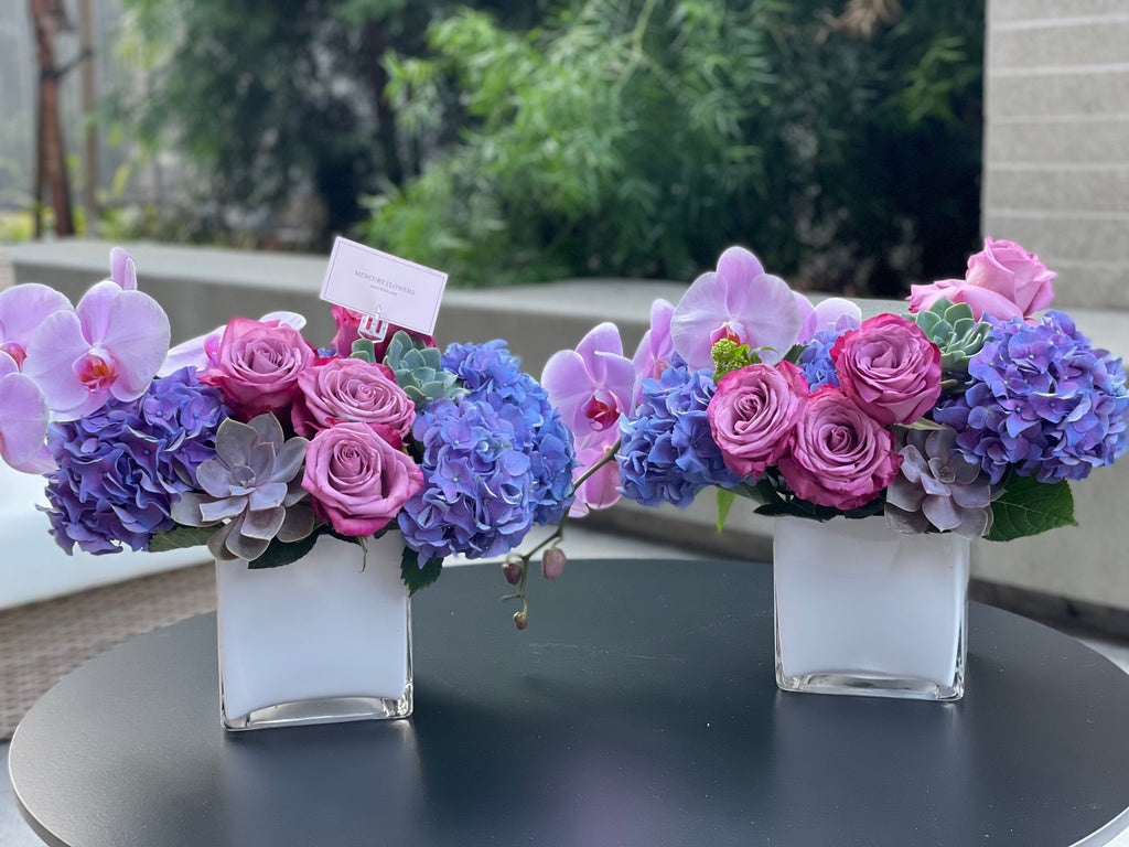 Arreglo floral con orquídea y suculentas en jarrón cuadrado de vidrio.