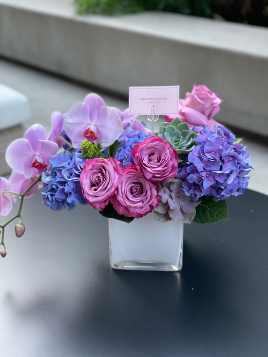 Flower arrangement with orchid and succulents in a glass square vase