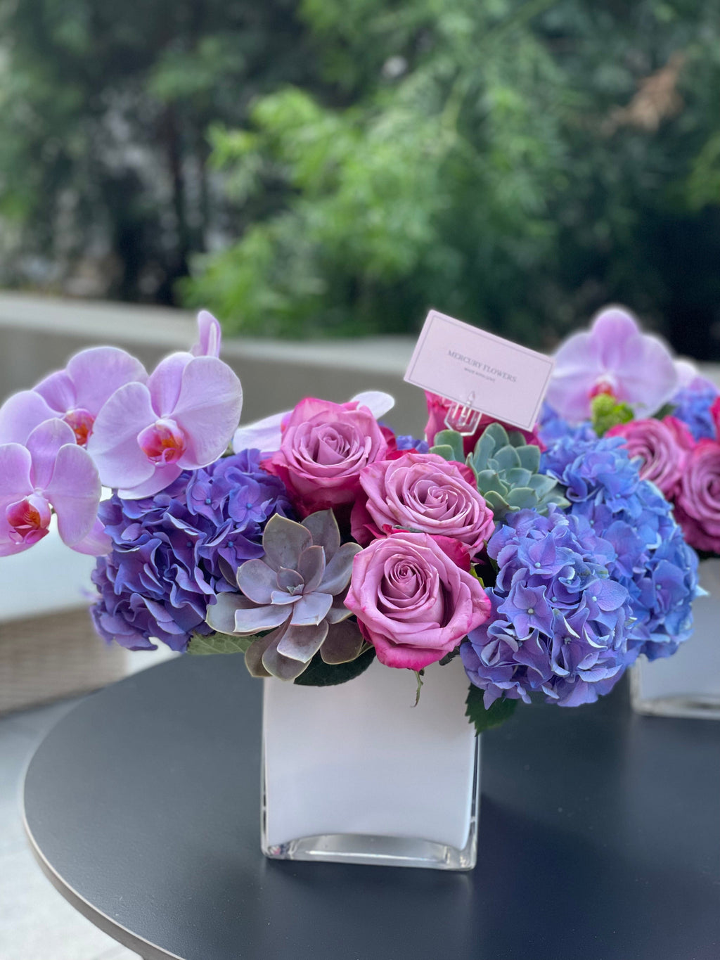 Arreglo floral con orquídea y suculentas en jarrón cuadrado de vidrio.